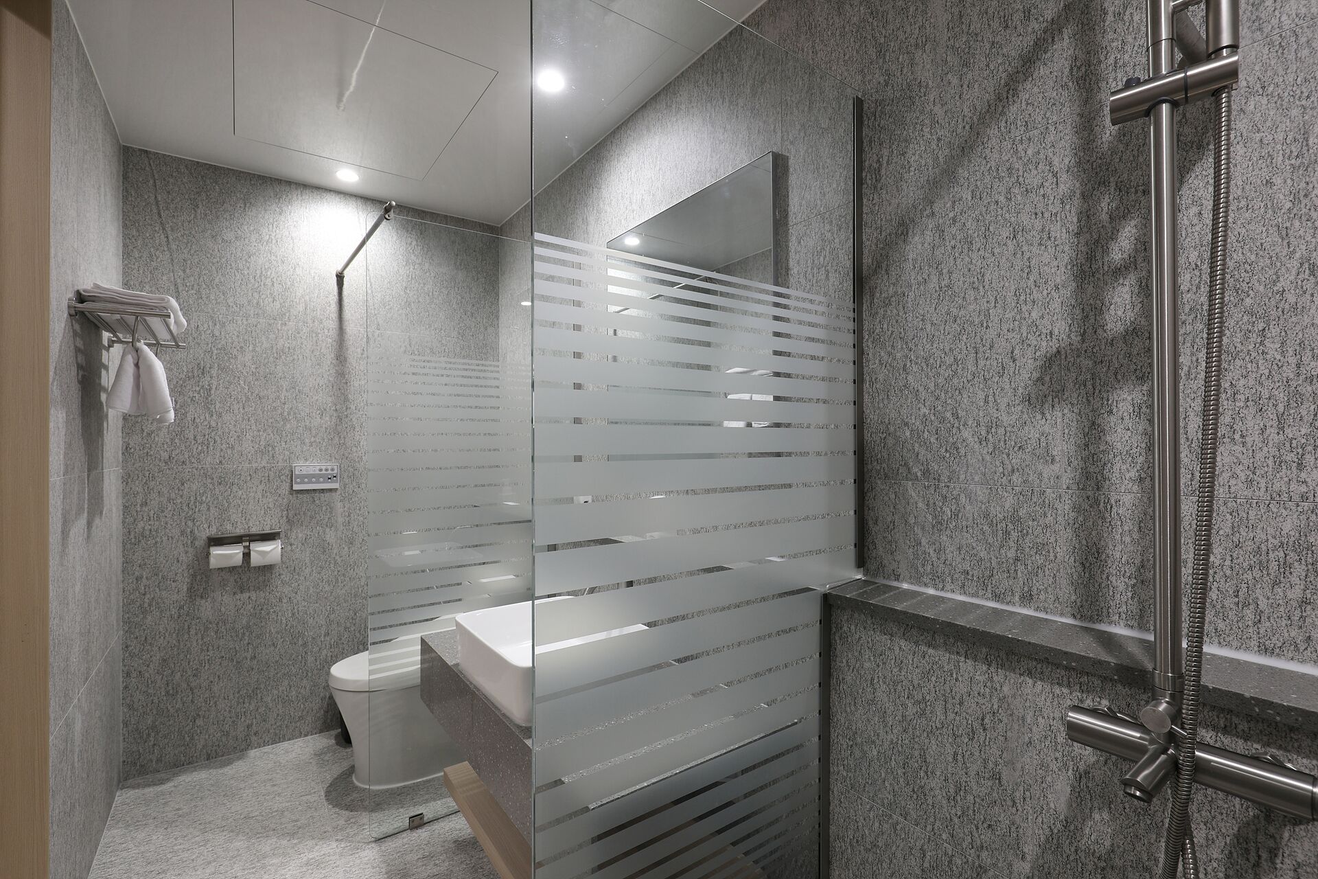 Een moderne badkamer met een glazen scheidingswand, toilet, wastafel en douche.