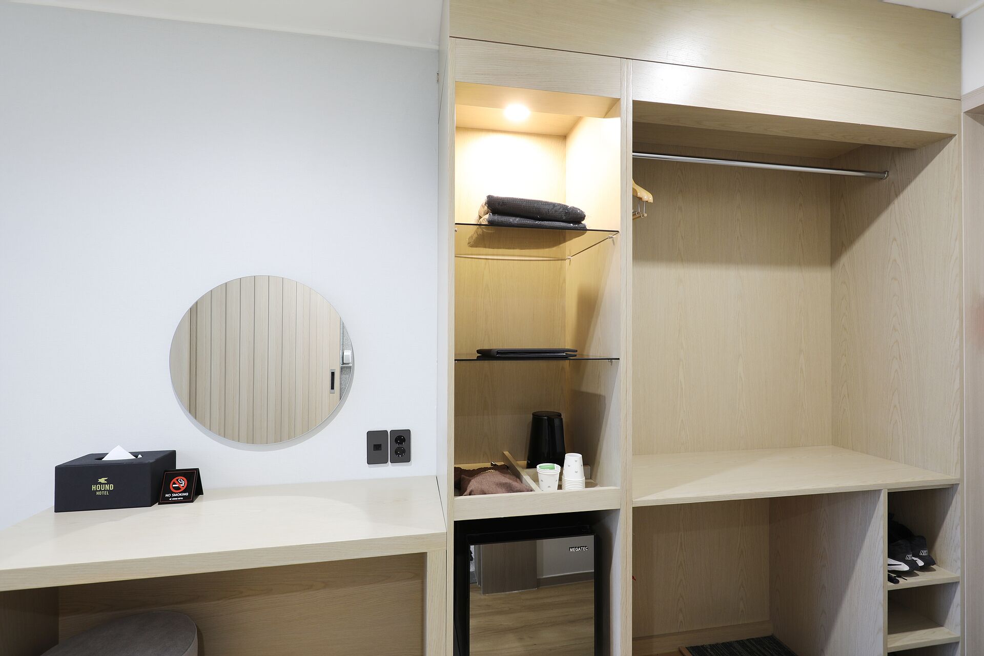 Une chambre d’hôtel équipée d’une armoire intégrée, d’un miroir rond, d’une table de chevet avec un boîte de mouchoirs et d’un panneau indiquant « Interdiction de fumer ».