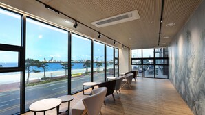 A modern interior with large windows, wooden flooring, and a view of a waterfront. - Pohang Hound Hotel Songdo Beach (Pohang)