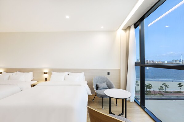 A modern hotel room with a large bed, a small table, and a chair. The room has a large window offering a view of the sea and a distant cityscape. - Pohang Hound Hotel Songdo Beach (Pohang)