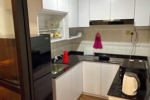 A kitchen with white cabinets, a black refrigerator, a red kettle, and a toaster. - Kuching City Center Riverbank Suites With Marvelous River View (Kuching Division)