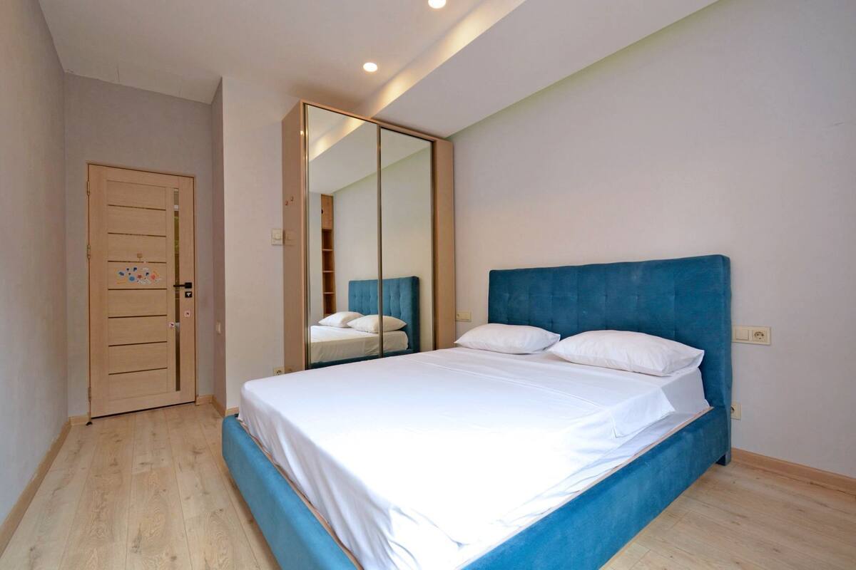 Ein Schlafzimmer mit einem Bett, einem Spiegel, einer Tür und einer Lampe.