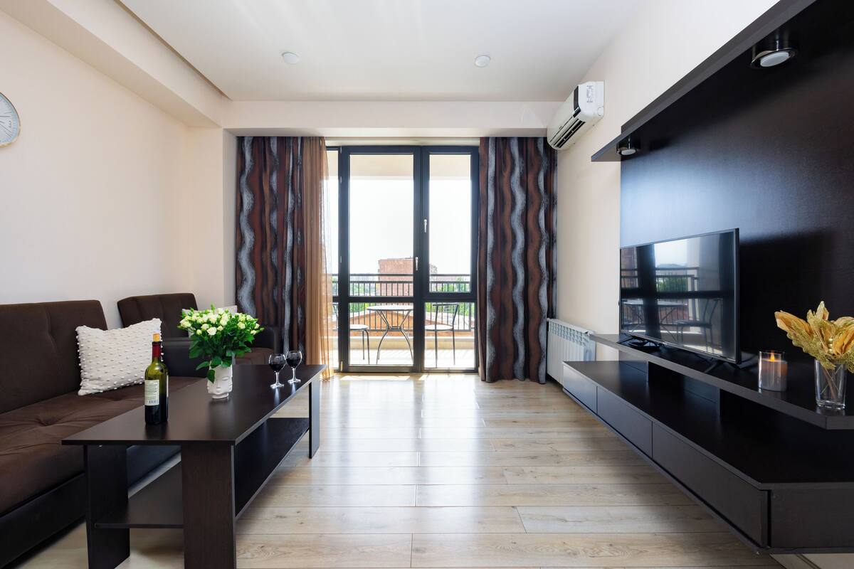 Ein modernes Wohnzimmer mit Sofa, Esstisch, Fernseher und Blick ins Freie.