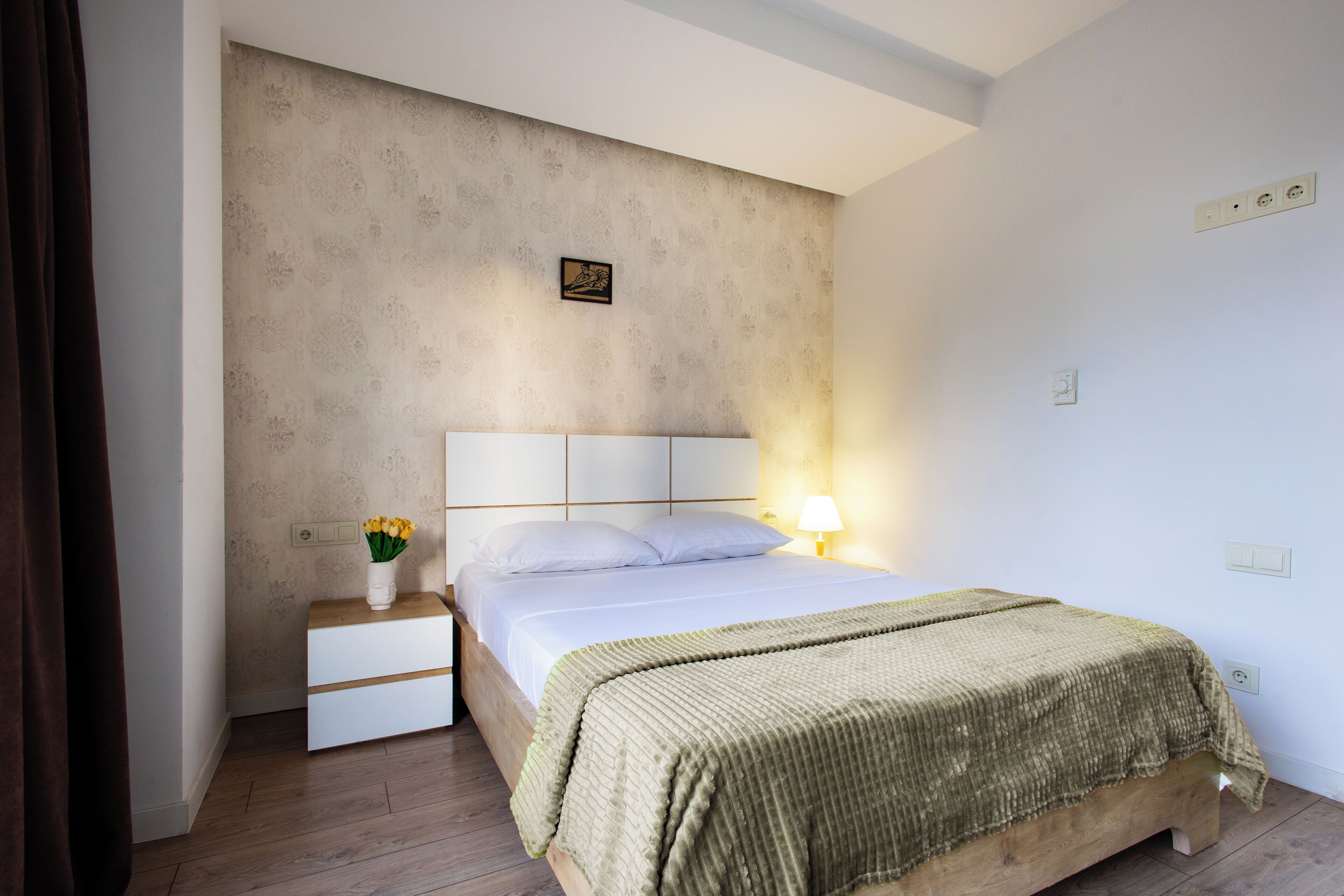 A bedroom with a bed, bedside table, and a nightstand with a vase of flowers.