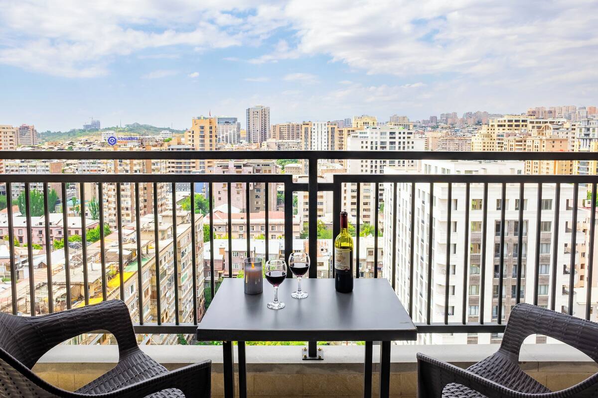 Ein Balkon mit Tisch, zwei Stühlen, einer Weinflasche und zwei roten Weingläsern.