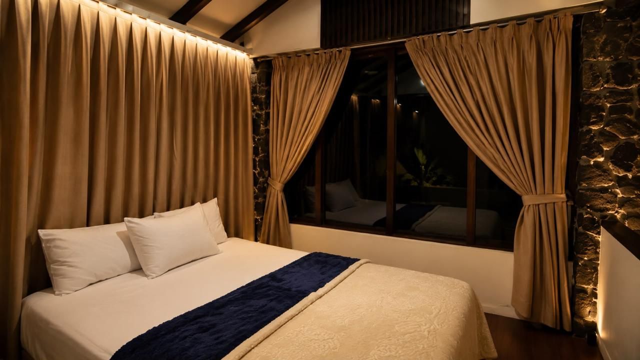Ein Bett mit blauem Akzent, beige Vorhängen und einer Steinwand.
