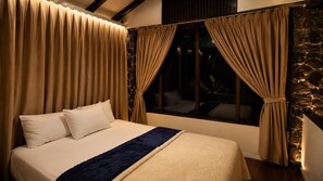A bed with a blue accent, beige curtains, and a stone wall.
