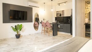A modern kitchen with a central island, a dining area with pink chairs, and a large flat-screen TV mounted on the wall. - w* | Modern 3BR AC Steps from Ciudad Amurallada (Cartagena de Indias)