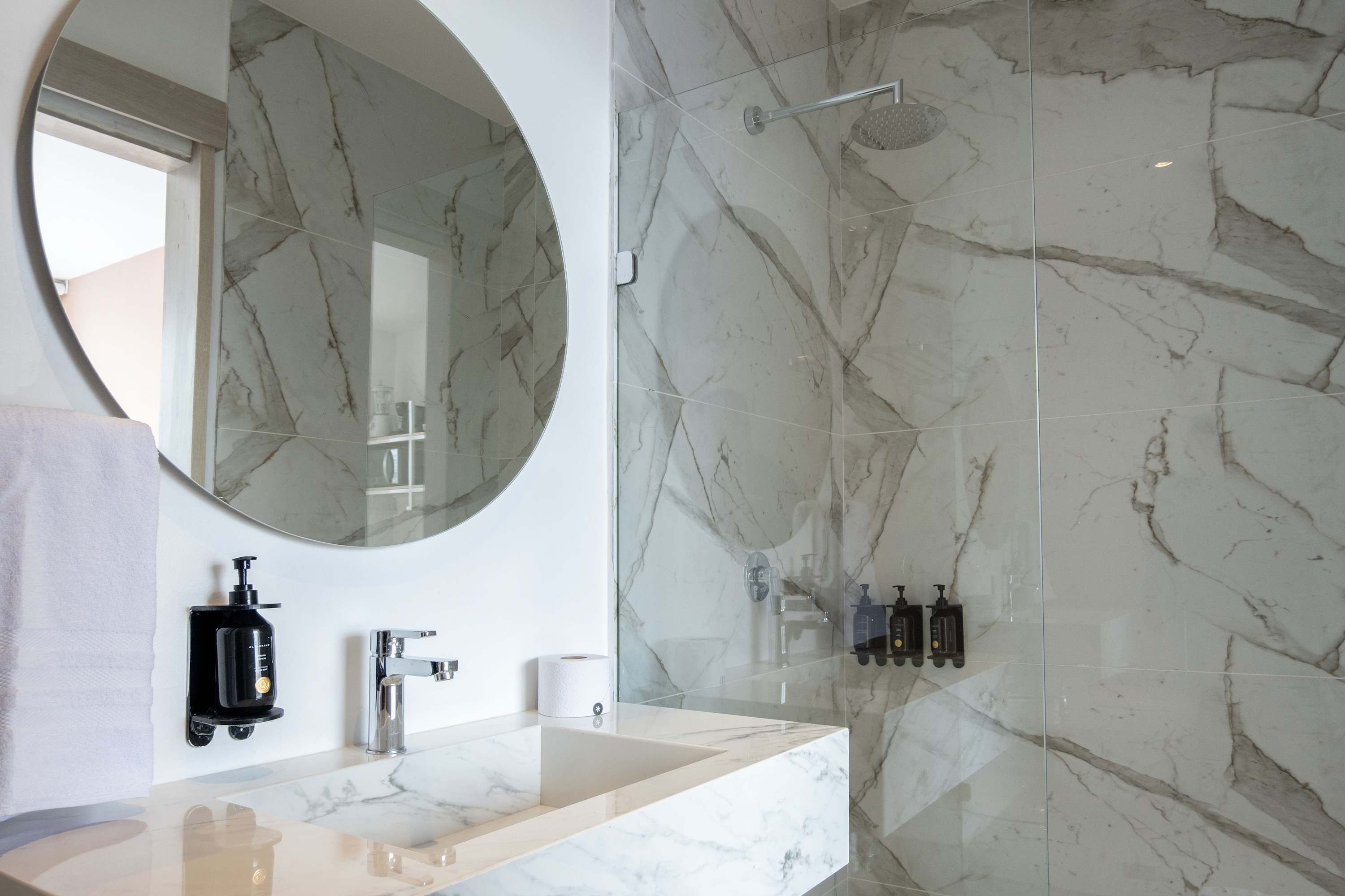 Une salle de bain moderne avec un meuble-lavabo en marbre, un grand miroir et une cabine de douche en verre.