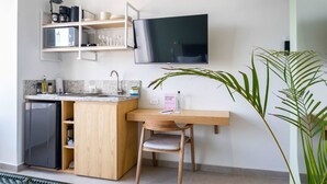 Een compacte keuken met een inbouwkoelkast, een houten eettafel en een aan de muur bevestigde televisie.