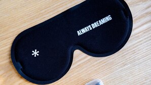 Een zwart slaapmasker met de tekst 'ALWAYS DREAMING' en een klein bakje met een witte deksel.