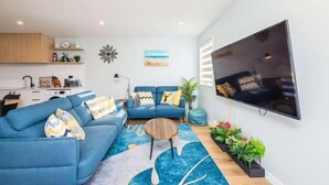 Ein modernes Wohnzimmer mit einem blauen Sofa, einem Couchtisch und einem an der Wand montierten Flachbildfernseher.