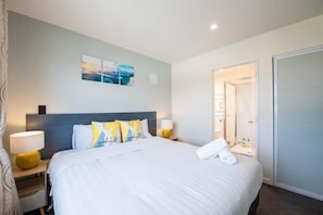 Habitación de hotel con una cama grande, una mesita de noche con lámpara, una obra de arte en la pared y una puerta que da al baño.