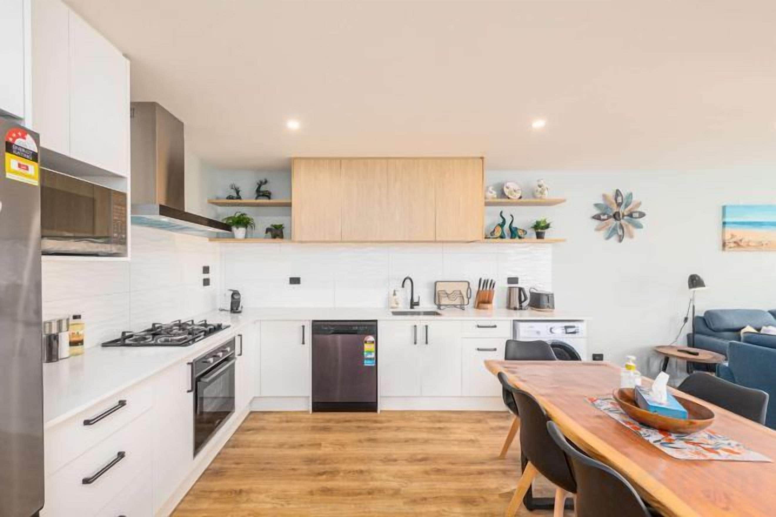 A modern kitchen with white cabinets, a wooden dining table, and a built-in oven.