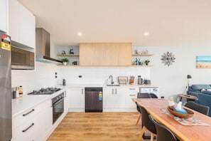 A modern kitchen with white cabinets, a wooden dining table, and a built-in oven. - 37 Galaxy B (Lake Tekapo)