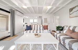 A modern living room with a white coffee table, striped sofas, and a view into the kitchen. - Moffat Beach Abode - Dog-friendly Escape by the Sea (Caloundra Region)
