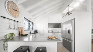 A modern kitchen with white cabinetry, a stainless steel refrigerator, and a large clock on the wall. - Moffat Beach Abode - Dog-friendly Escape by the Sea (Caloundra Region)