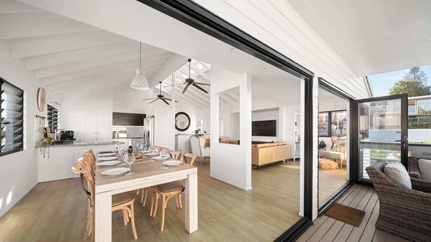 A spacious kitchen with modern appliances, a dining area with wooden furniture, and a large sliding glass door leading to an outdoor seating area. - Moffat Beach Abode - Dog-friendly Escape by the Sea (Caloundra Region)