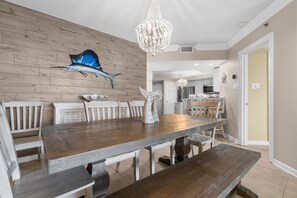 A dining area with a wooden table and benches, a chandelier, and a wall-mounted sculpture. - Beachfront 3 Bed Ground Floor at Summer House in OB! Free Daily Activities! (Orange Beach)