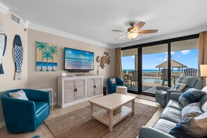 A living room with a television, a ceiling fan, and a view of the ocean.
