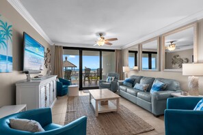Ein großzügiger Wohnraum mit einer großen Couch, zwei Sesseln, einem Couchtisch und einem Fernseher. Es gibt einen Balkon mit Meerblick.