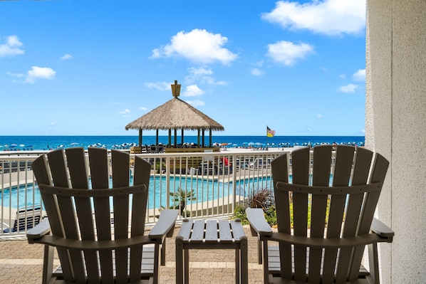 Blick auf einen Pool mit zwei Adirondack-Stühlen, einem Reetdach-Pavillon und Blick auf das Meer.