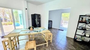 A spacious room with a large table, chairs, a refrigerator, and a shelving unit.
