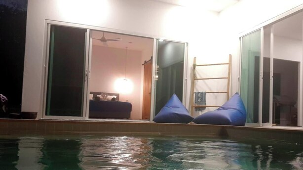 A swimming pool with blue bean bags and a sliding glass door leading to a room.