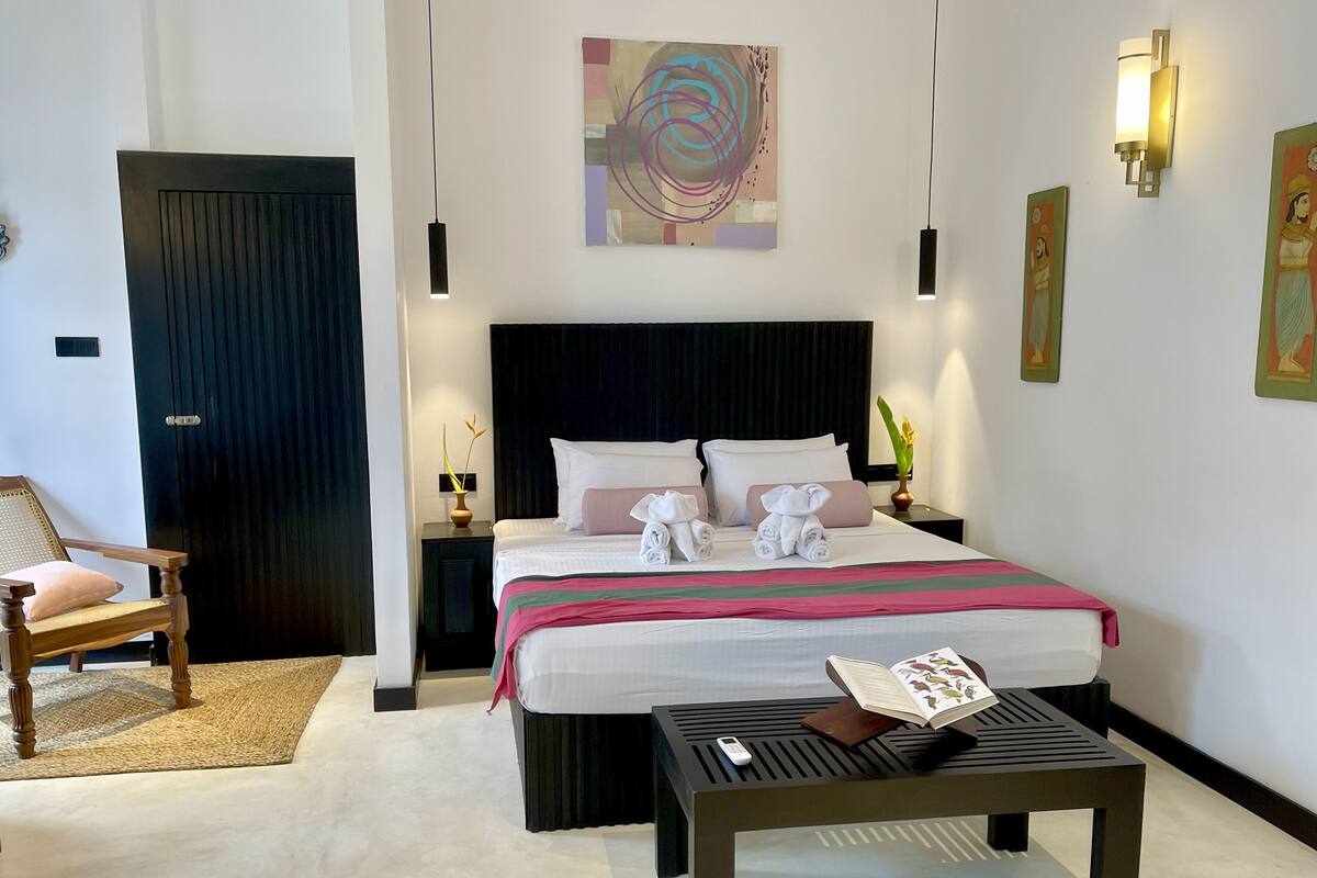Een hotelkamer met een groot bed, een houten stoel, een klein tafeltje en een schilderij aan de muur.