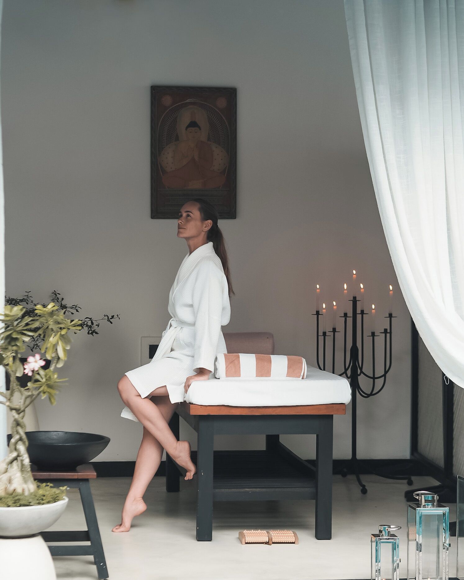 Una persona sentada en un banco en una habitación con un cuadro de Buda, un candelabro y una planta en maceta.