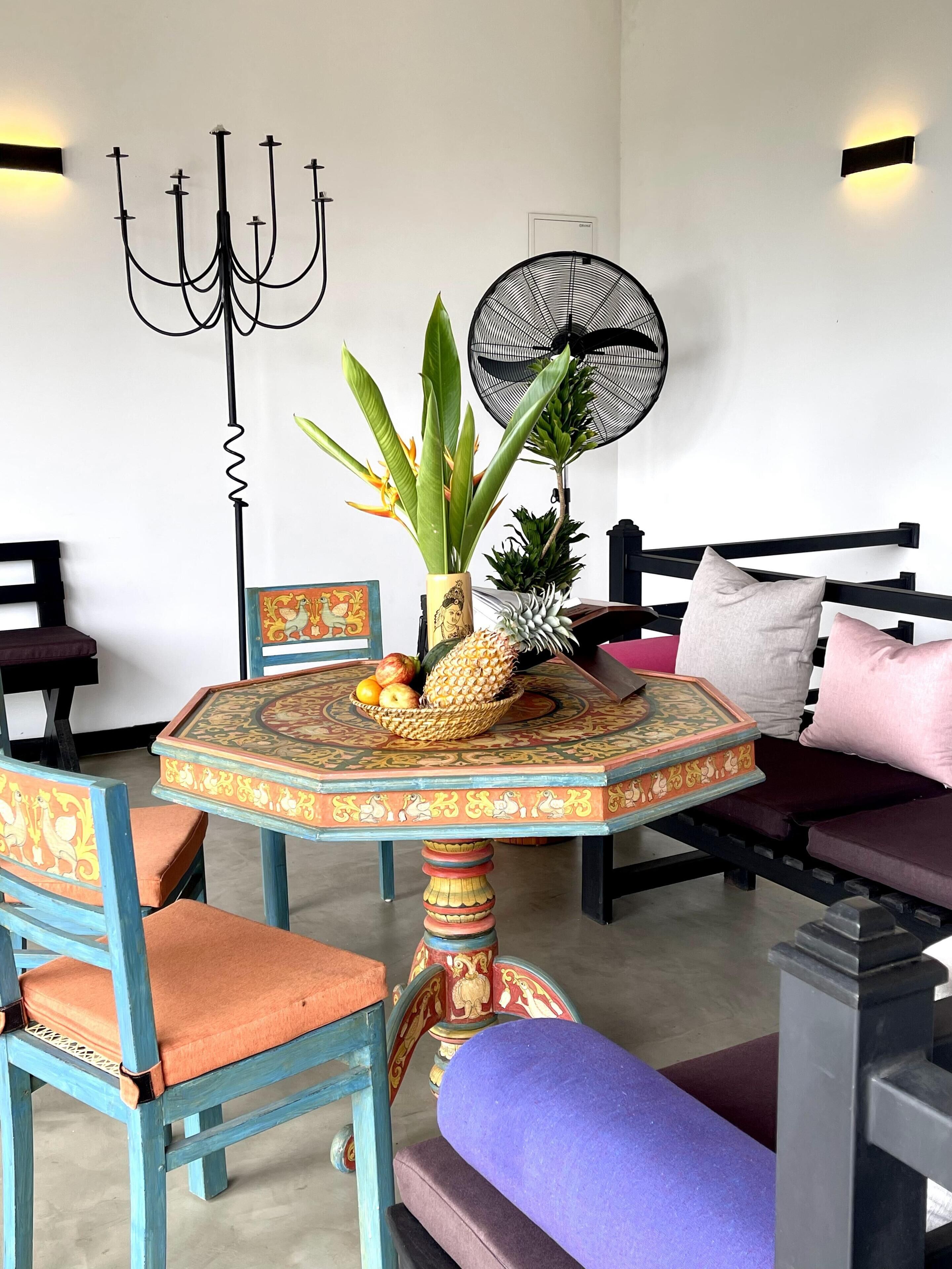 A dining area with a round table, chairs, a wall-mounted fan, and a decorative wall piece.