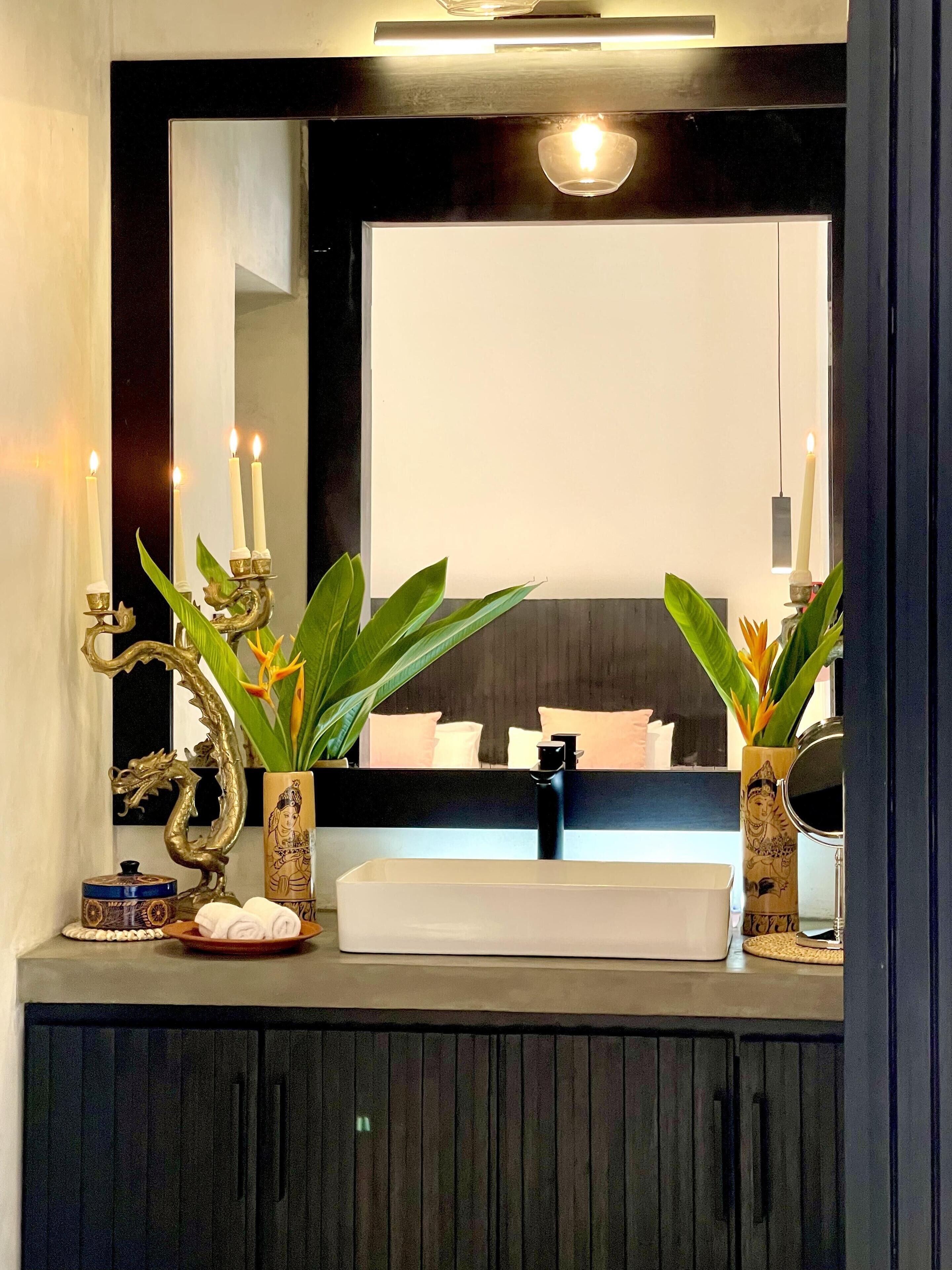 A bathroom vanity with a mirror, a sink, and decorative items including a candelabra and plants.