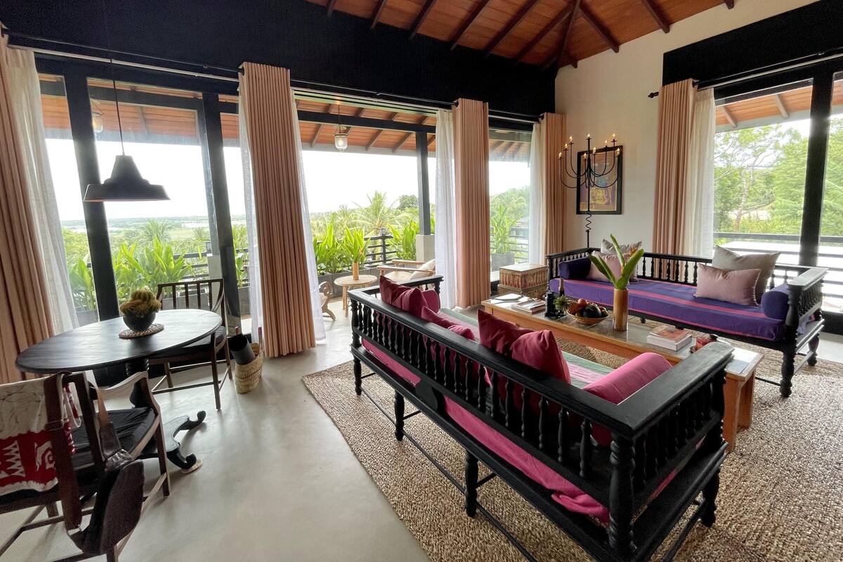 Een ruime woonkamer met een bank, een eettafel en uitzicht op weelderige begroeiing.