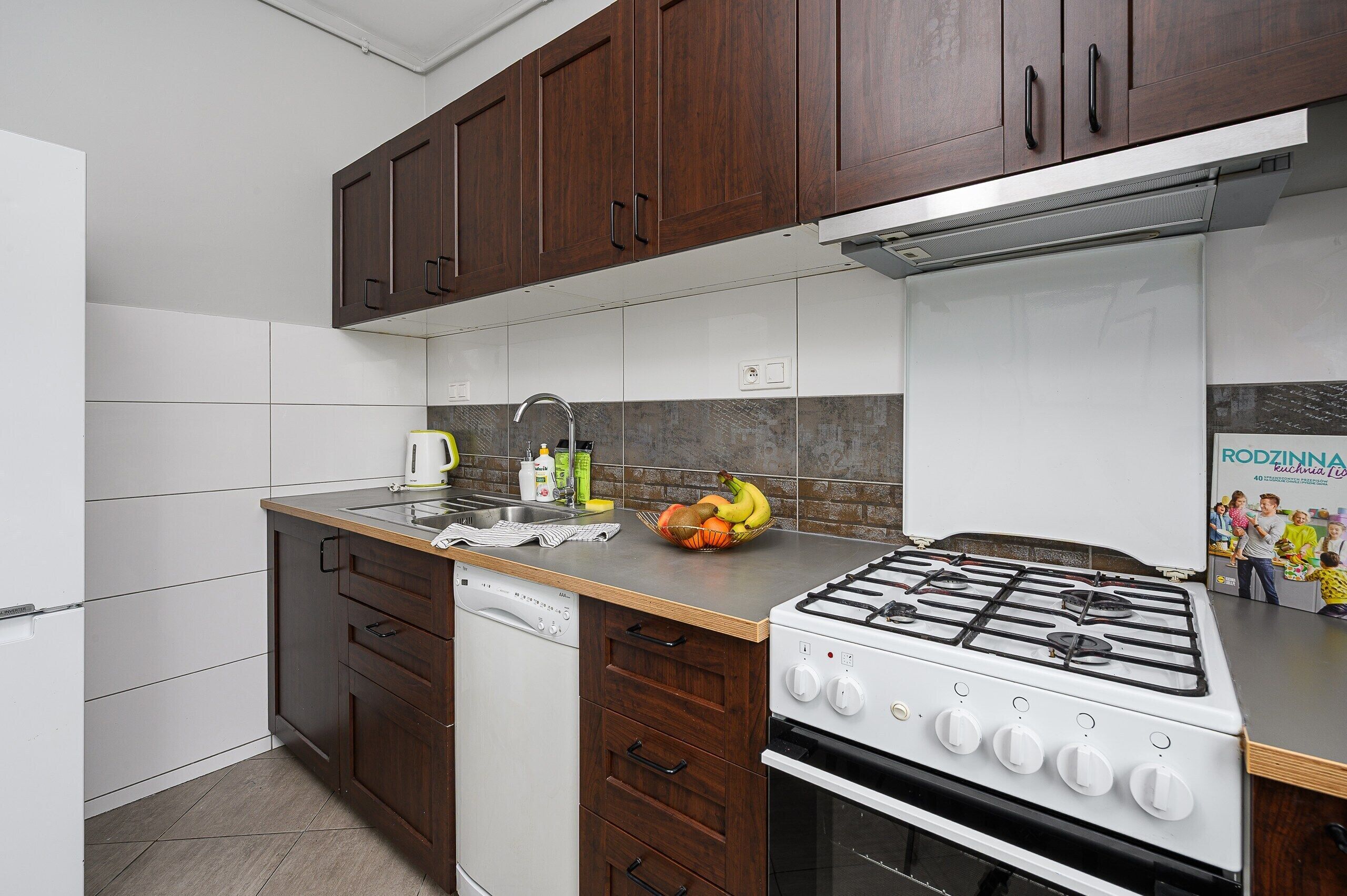 Una cocina moderna con gabinetes de madera oscura, lavavajillas blanco, estufa a gas y salpicadero de azulejos.