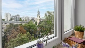 A view from a window overlooking a cityscape with modern buildings and a church with a tower. - City center Apart near Palace of Culture (Warsaw)