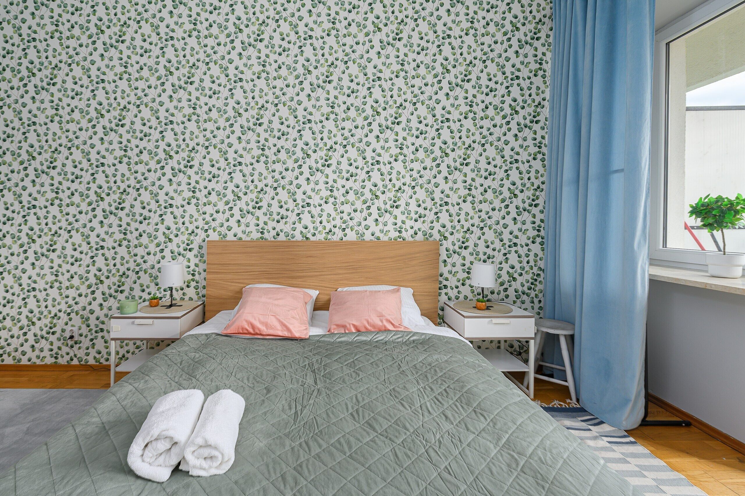 A neatly made bed with a green quilt, two pink pillows, and a pair of folded white towels.