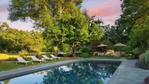 Ein Swimmingpool mit Liegestühlen und Sonnenschirmen, umgeben von Bäumen und viel Grün.