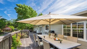 Eine Holzterrasse mit Esstisch, Stühlen, Sonnenschirm und Grillplatz.