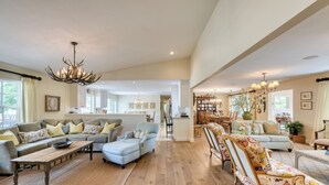 Ein großzügiges Wohnzimmer mit Holzboden, einer Sofagarnitur, einem Essbereich mit einer Deckenleuchte und einer Küche im Hintergrund.