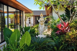 A tropical garden with a statue, lush greenery, and a modern building with large windows. - Villa Vidrev - Private Infinity Pool & Rice Fields by BaliSuperHost (Bali)