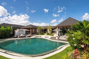 A swimming pool surrounded by a well-maintained lawn, with a building in the background. - Villa Vidrev - Private Infinity Pool & Rice Fields by BaliSuperHost (Bali)