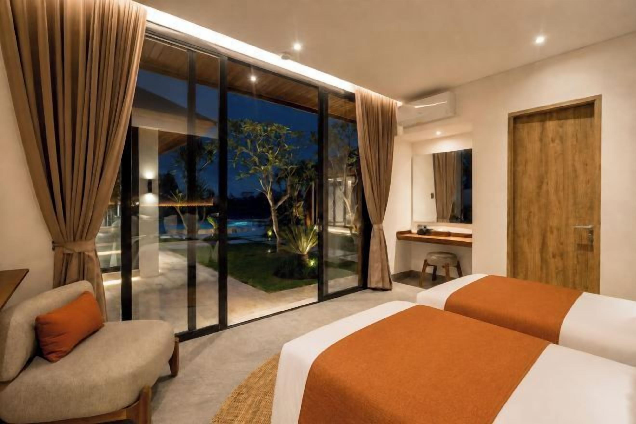 A hotel room with a large sliding glass door leading to a balcony, a bed with a striped blanket, a chair, and a small table with a mirror.
