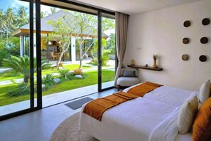 A bedroom with a large bed, a view of a garden, and a sliding glass door leading outside. - Villa Vidrev - Private Infinity Pool & Rice Fields by BaliSuperHost (Bali)