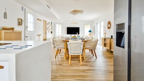 Une cuisine moderne dotée d’un îlot central, d’un coin repas avec une table ronde et des chaises, et d’un téléviseur encastré.