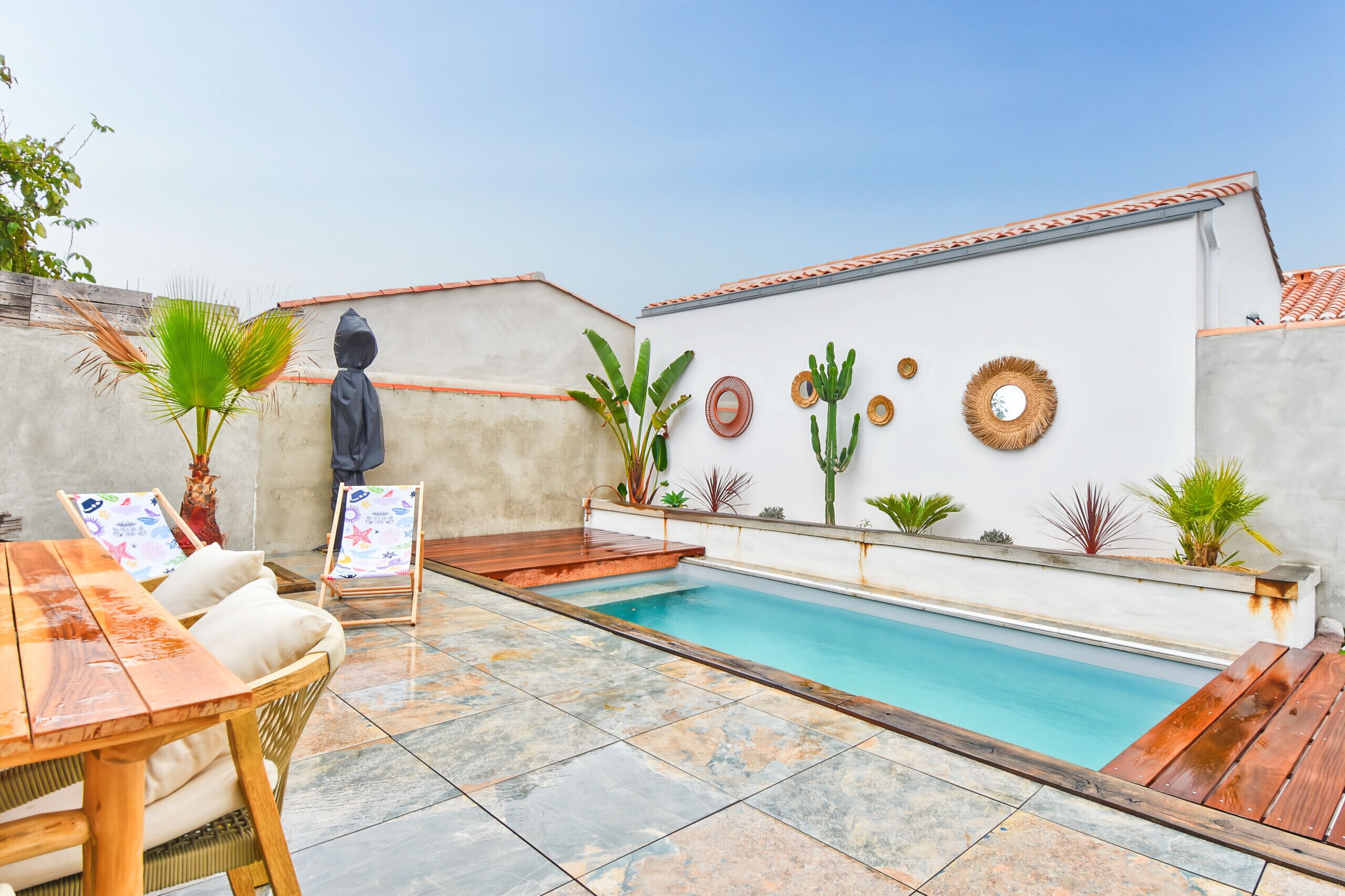 Área de piscina en la azotea con terraza de madera, asientos y diversas plantas.