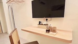 A modern room with a mounted TV, a wooden desk, a chair, and a small shelf with decorative items. - ONE18 Boutique Hotel (Kuala Lumpur)