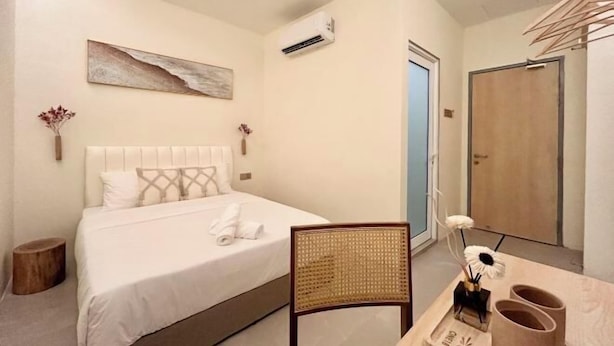 A bedroom with a bed, a chair, a small table with a vase and slippers, and a door. - ONE18 Boutique Hotel (Kuala Lumpur)