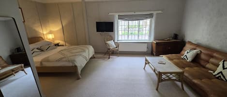 A room with a bed, a sofa, a small table, a chair, a television, and a window with a view outside.