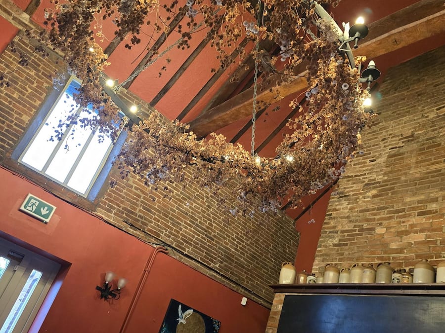 A restaurant interior with brick walls, a hanging floral arrangement, a mural, and a brick oven.