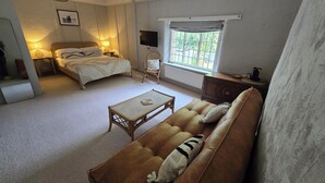 A cozy room with a bed, a sofa, a small table, and a chair. There is a window with a view of greenery outside. - The Ostrich (Castle Acre)
